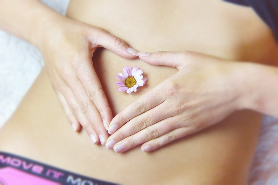 A girl's tummy with her hand in a heart shape with a flower in her belly button